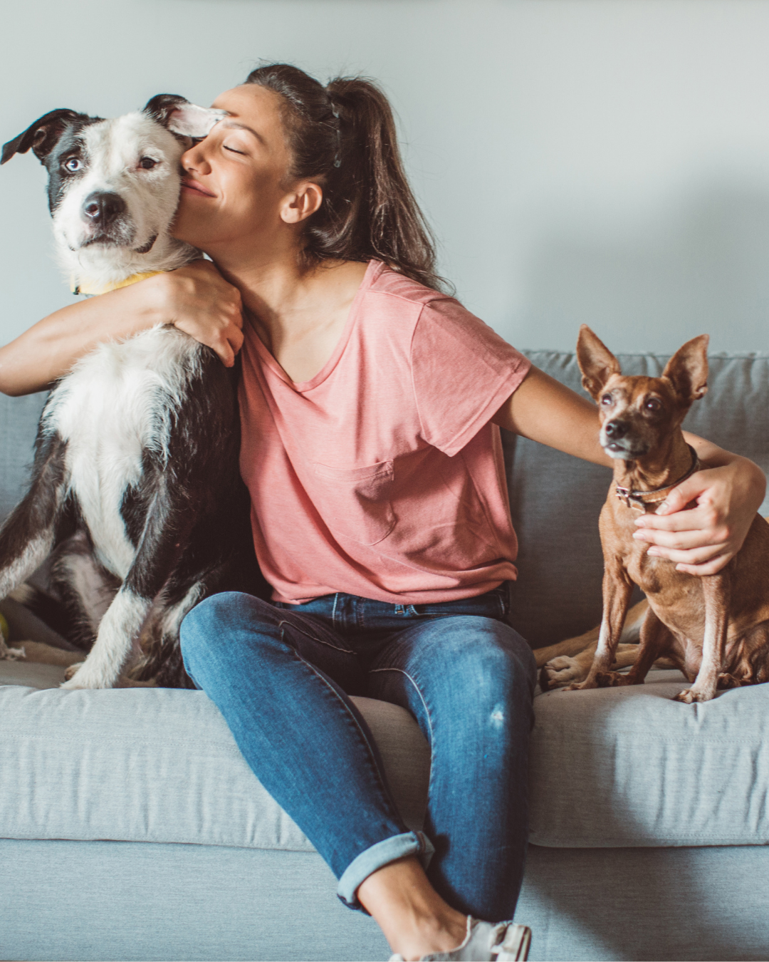 Woman at home with her two dogs, sharing a joyful moment on the couch