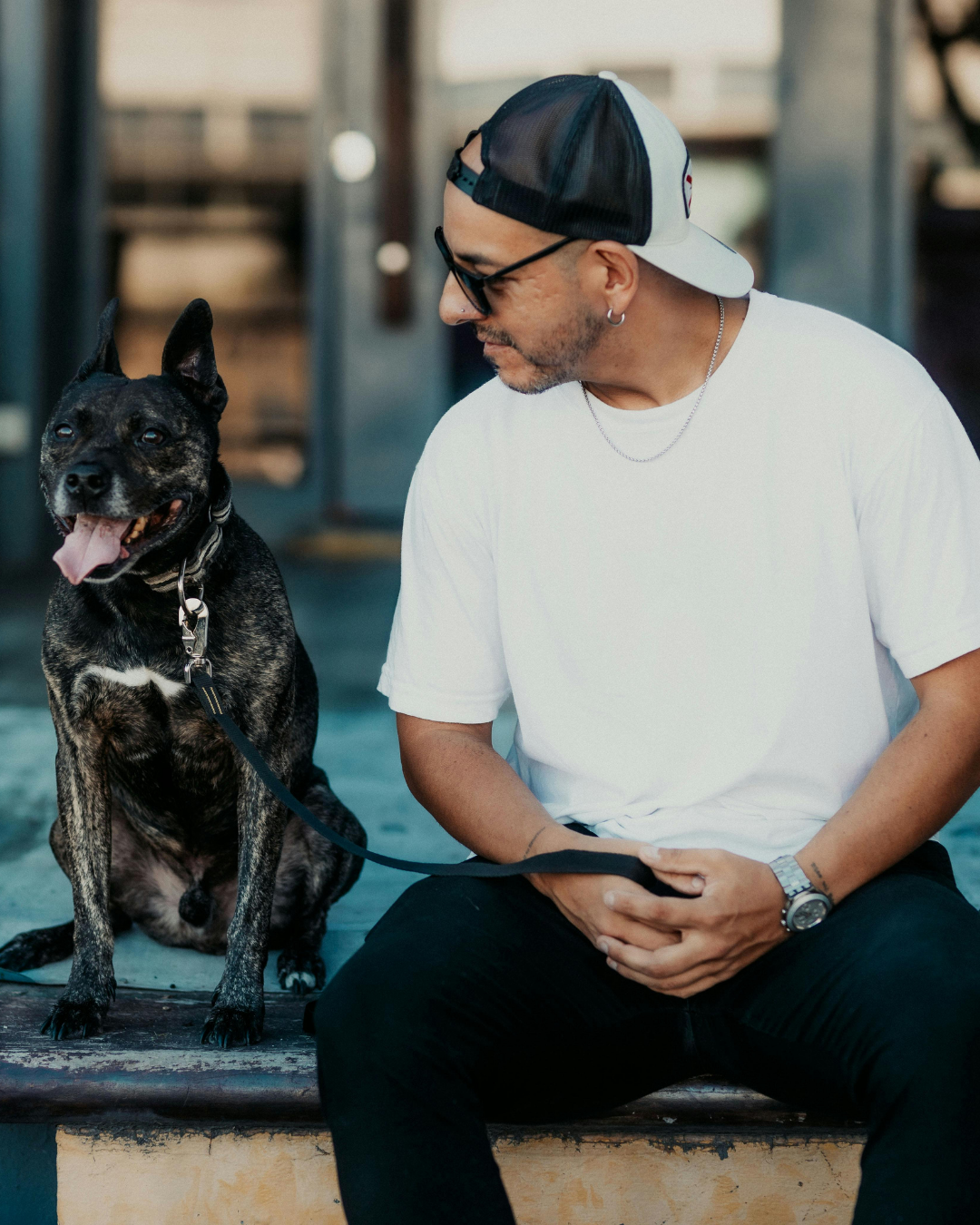 Man sitting with his black dog in an urban setting, looking at each other