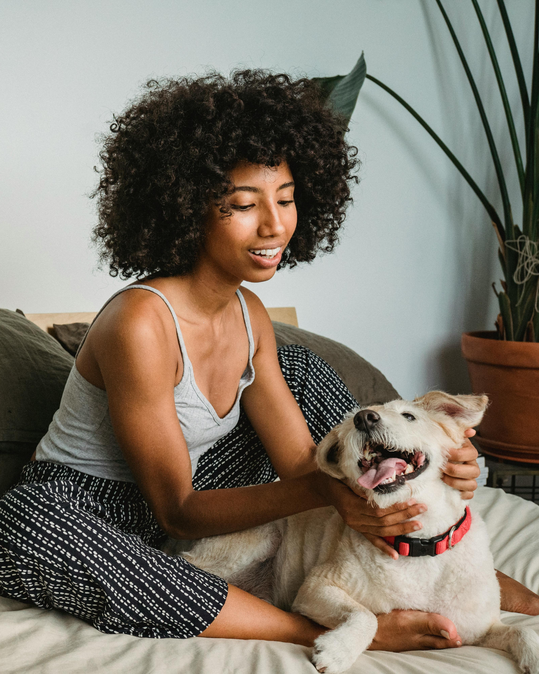 Woman smiling as her dog plays happily beside her on the bed